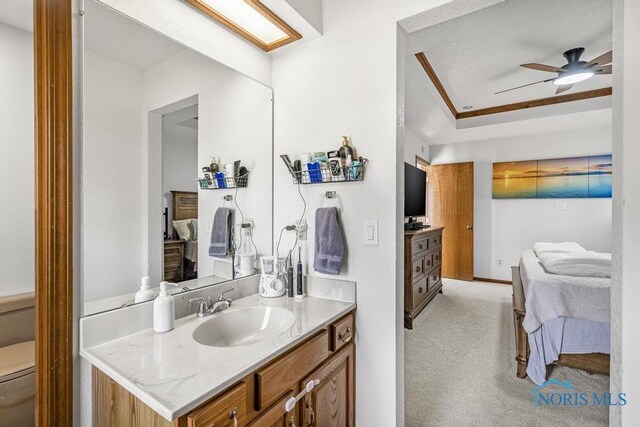 ensuite bathroom featuring ceiling fan, toilet, ensuite bathroom, vanity, and a raised ceiling