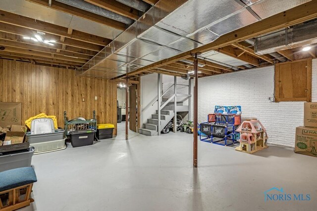 unfinished below grade area featuring wooden walls, brick wall, and stairs