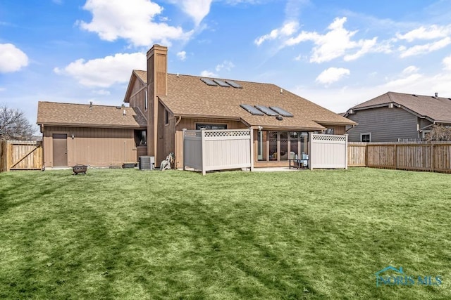 rear view of property with a yard, central air condition unit, a chimney, and a fenced backyard