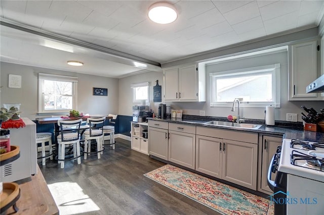 kitchen featuring dark countertops, dark wood-style flooring, white gas range, and a sink