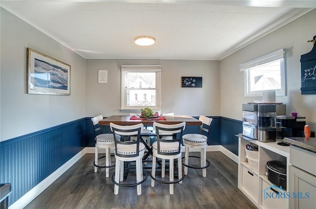 dining space with dark wood finished floors, a wainscoted wall, and ornamental molding