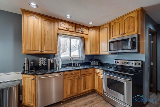 kitchen featuring light wood finished floors, recessed lighting, dark stone countertops, stainless steel appliances, and a sink