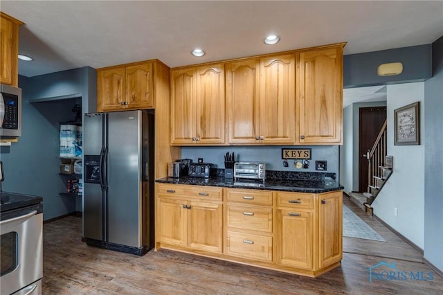 kitchen featuring dark stone countertops, stainless steel appliances, wood finished floors, and recessed lighting