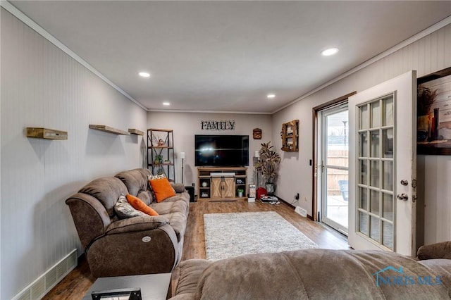 living room featuring visible vents, baseboards, wood finished floors, and ornamental molding