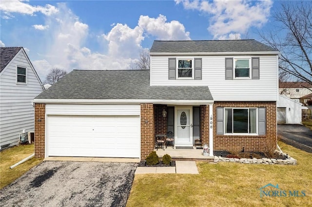 traditional-style house with brick siding, driveway, an attached garage, and a front yard