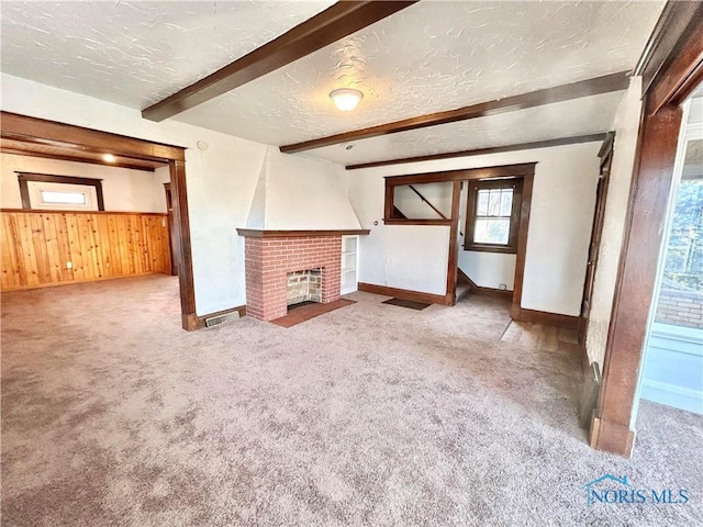 unfurnished living room featuring beam ceiling, a brick fireplace, carpet floors, and a textured ceiling