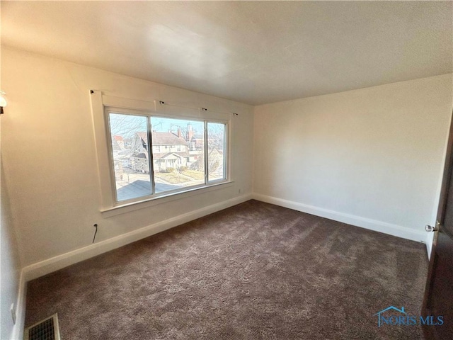 empty room featuring visible vents, baseboards, and dark carpet