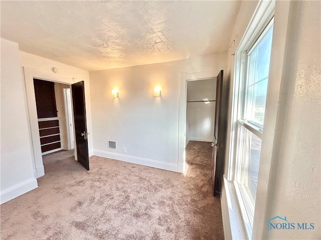 unfurnished bedroom featuring a textured ceiling, carpet, visible vents, and baseboards