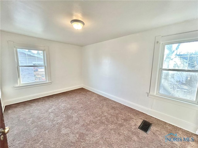 spare room with visible vents, dark carpet, plenty of natural light, and baseboards