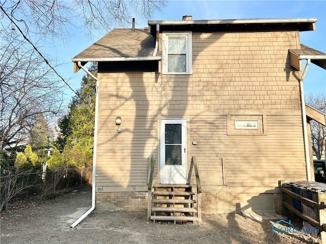 back of house featuring fence, roof with shingles, and entry steps