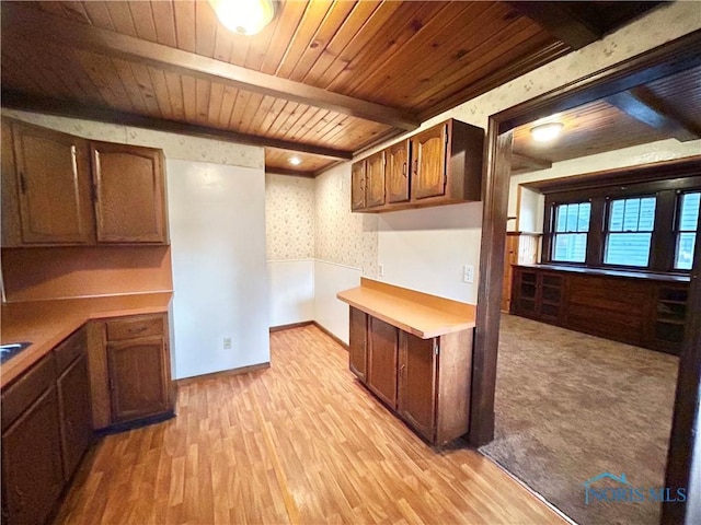 kitchen with wallpapered walls, light countertops, light wood-style floors, wooden ceiling, and beamed ceiling