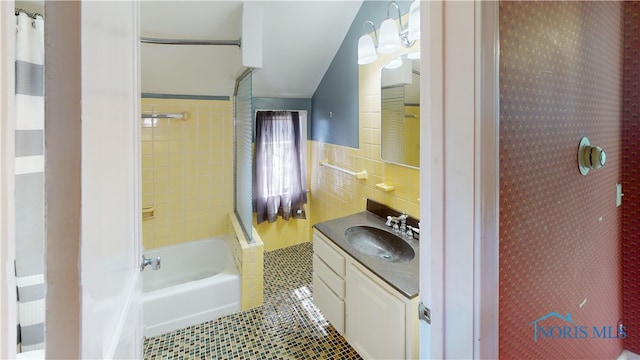 full bathroom with vanity, a wainscoted wall, shower / bath combination with curtain, tile walls, and tile patterned floors