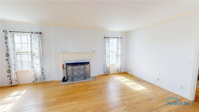 unfurnished living room featuring ornamental molding, a tile fireplace, baseboards, and wood finished floors