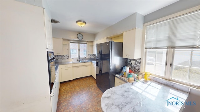 kitchen featuring decorative backsplash, a sink, black appliances, and stainless steel counters