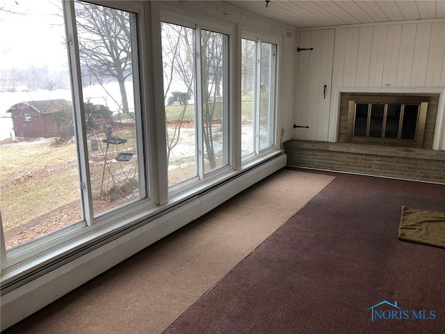 unfurnished living room with a baseboard heating unit, wooden walls, a glass covered fireplace, and carpet