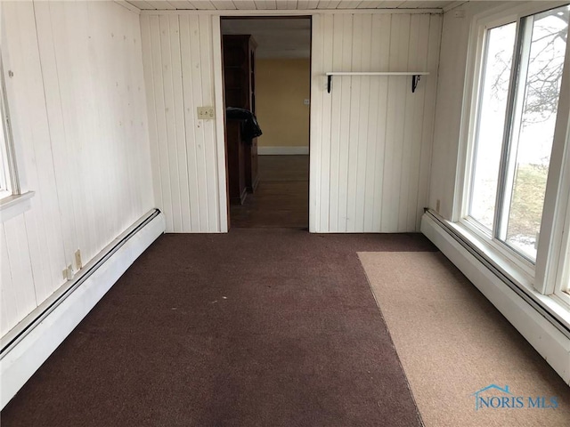 carpeted spare room with wood walls and baseboard heating