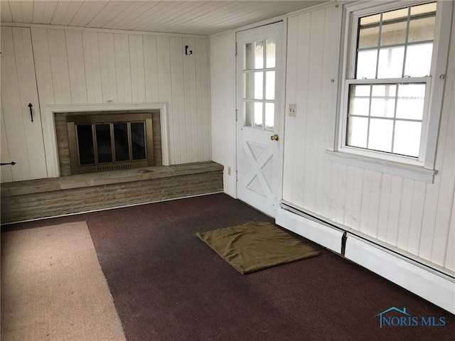 unfurnished living room featuring wood walls, a baseboard heating unit, wood ceiling, a brick fireplace, and carpet flooring