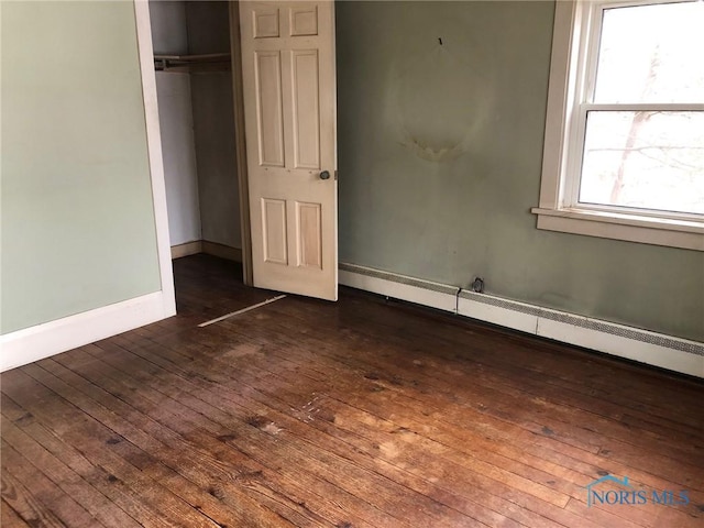 unfurnished bedroom featuring baseboard heating, baseboards, dark wood-type flooring, and a closet