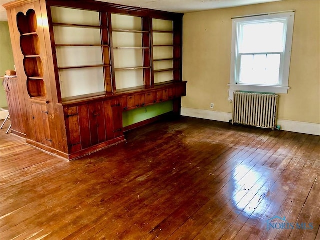 empty room with hardwood / wood-style flooring, radiator, and baseboards