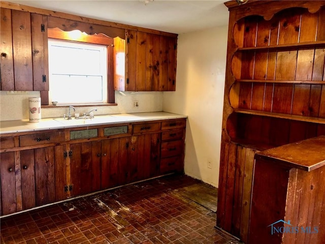 kitchen with a sink, baseboards, open shelves, light countertops, and brick patterned floor