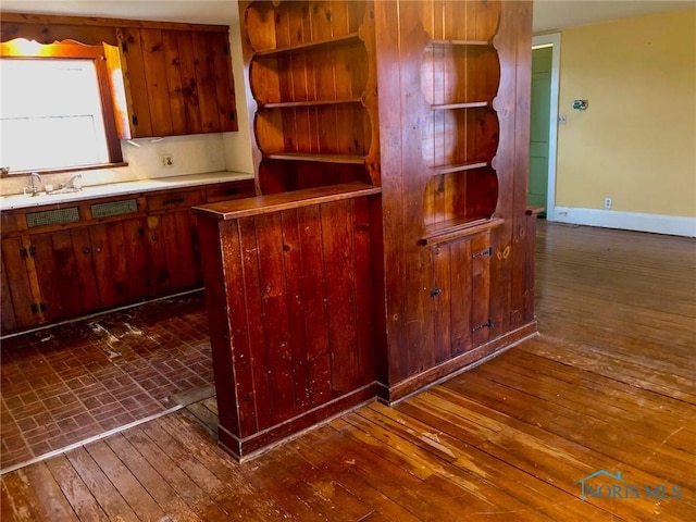 kitchen with dark wood-type flooring, light countertops, baseboards, and a sink