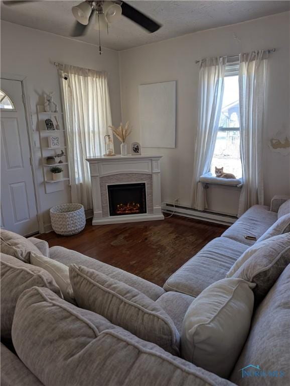 living area with baseboard heating, a fireplace with raised hearth, ceiling fan, and wood finished floors