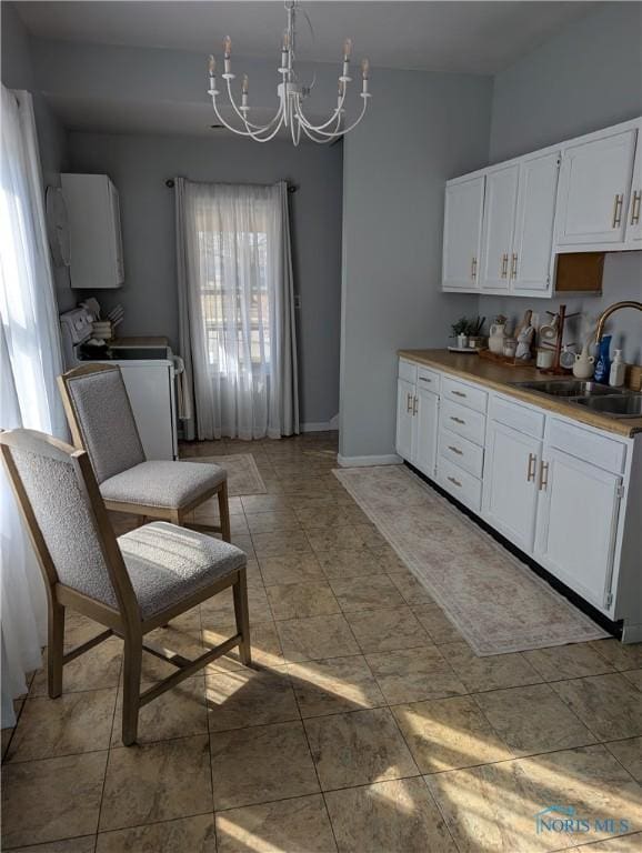 kitchen with baseboards, a sink, stove, white cabinets, and a chandelier