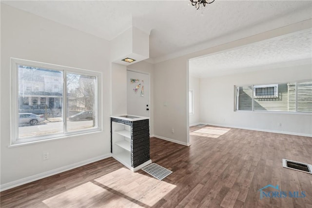 unfurnished living room featuring a textured ceiling, wood finished floors, visible vents, and baseboards