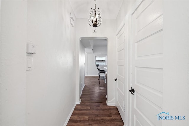 hall featuring dark wood finished floors, a notable chandelier, baseboards, and arched walkways