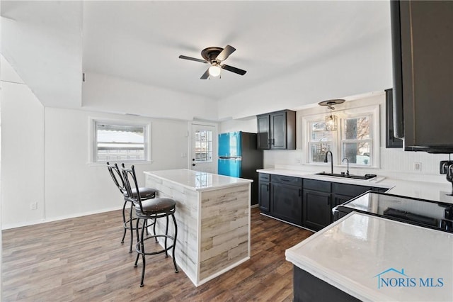 kitchen featuring a kitchen bar, a sink, a kitchen island, dark wood-style floors, and light countertops