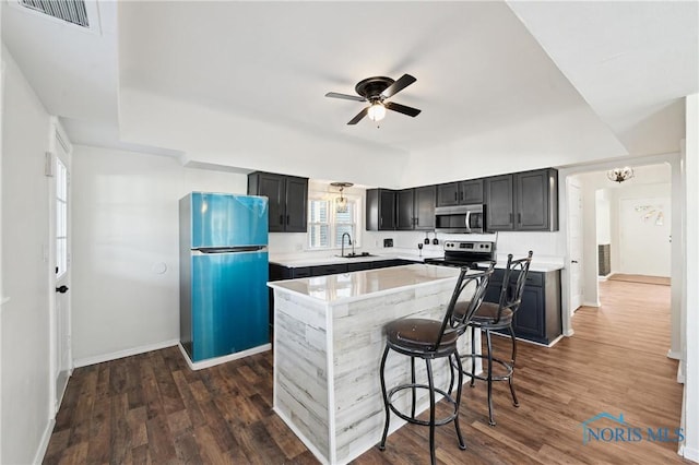 kitchen featuring visible vents, a kitchen island, appliances with stainless steel finishes, dark wood-style floors, and a sink