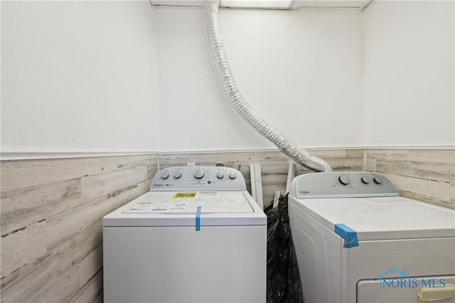 washroom featuring laundry area, separate washer and dryer, and a wainscoted wall