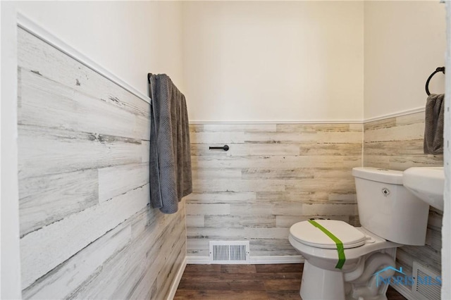 bathroom featuring wood finished floors, visible vents, wood walls, wainscoting, and toilet