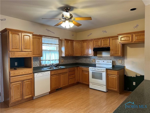 kitchen featuring under cabinet range hood, white appliances, dark countertops, and light wood-style flooring