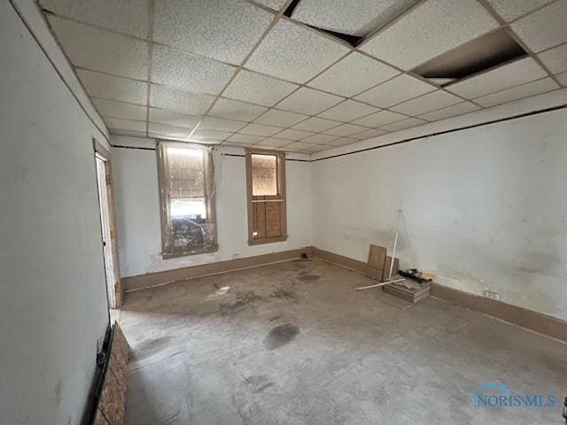 empty room featuring a paneled ceiling, baseboards, and concrete floors