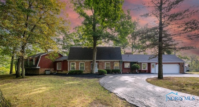 view of front of property featuring a gambrel roof, a lawn, driveway, an attached garage, and brick siding