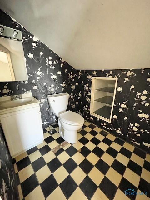 bathroom with tile patterned floors, toilet, wallpapered walls, vanity, and vaulted ceiling