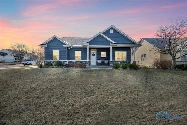 craftsman-style home with stone siding, a lawn, and a porch