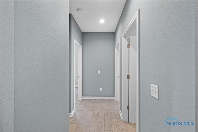 corridor featuring light wood-style flooring, a textured wall, and baseboards