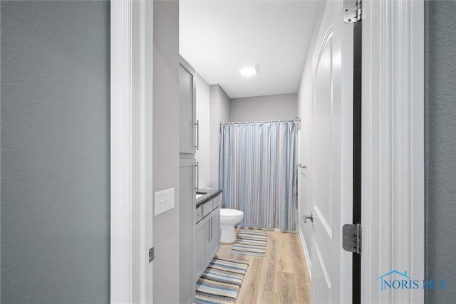 full bathroom with a shower with curtain, toilet, wood finished floors, vanity, and a textured wall