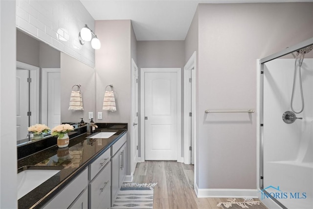 bathroom with a shower stall, wood finished floors, double vanity, and a sink