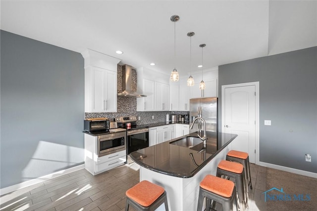 kitchen with wall chimney range hood, a breakfast bar area, decorative backsplash, appliances with stainless steel finishes, and a sink