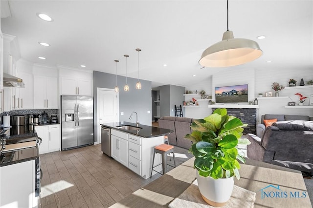 kitchen featuring dark countertops, open floor plan, appliances with stainless steel finishes, wood finished floors, and a sink