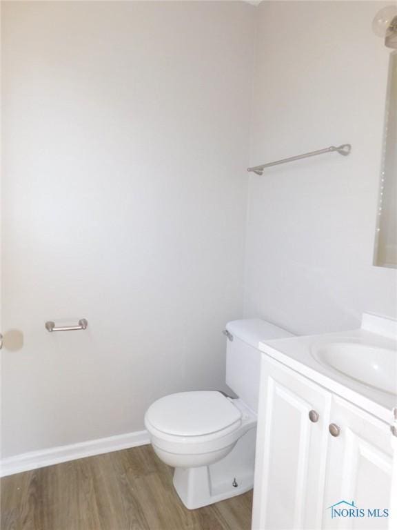 half bathroom with toilet, vanity, baseboards, and wood finished floors