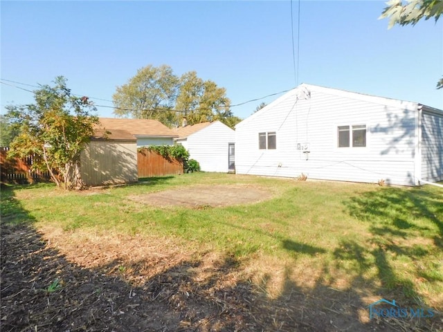 rear view of house with an outbuilding, a lawn, and fence