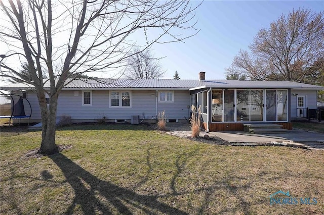 rear view of house featuring a trampoline, metal roof, a chimney, a sunroom, and a patio area