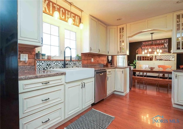 kitchen featuring wood finished floors, a sink, glass insert cabinets, stainless steel dishwasher, and backsplash