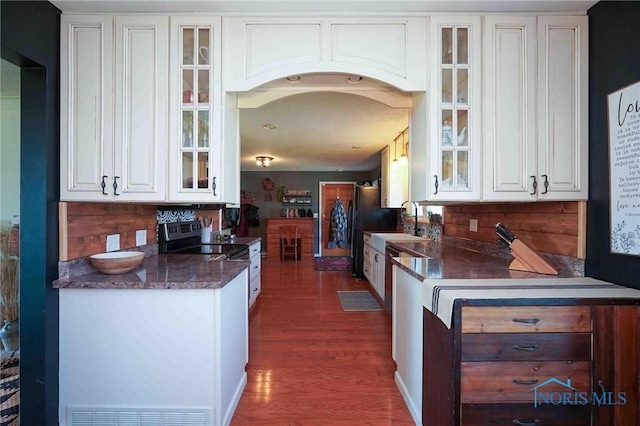 kitchen with arched walkways, stainless steel range with electric stovetop, white cabinetry, and glass insert cabinets