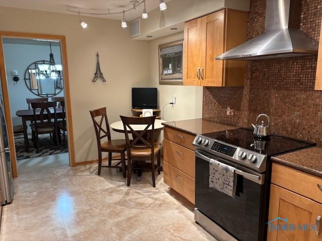 kitchen with tasteful backsplash, stainless steel electric stove, rail lighting, wall chimney range hood, and baseboards