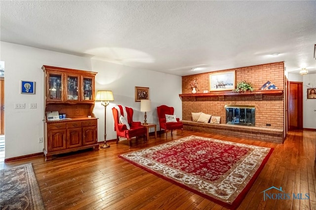 living room featuring baseboards, wood-type flooring, a textured ceiling, and a brick fireplace